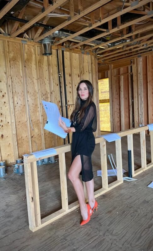 Confident woman in stylish black dress at construction site, highlighting empowerment and professionalism.