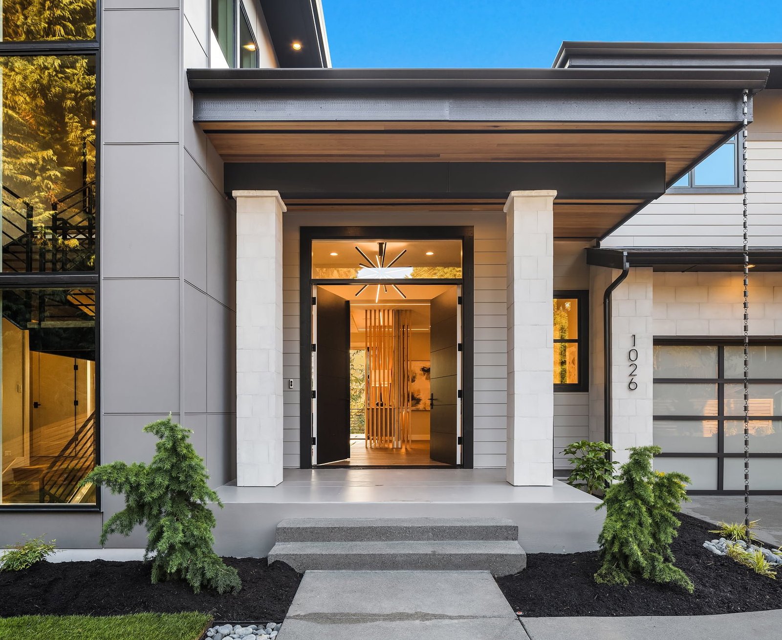 Elegant modern home entrance with striking porch, double doors, and lush landscaping.