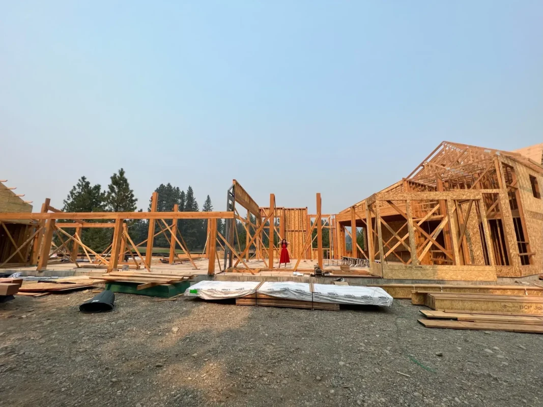 Framing stage of a house under construction surrounded by nature and materials.