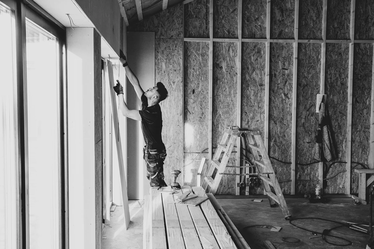 Construction worker skillfully installing drywall in an unfinished interior space filled with tools.