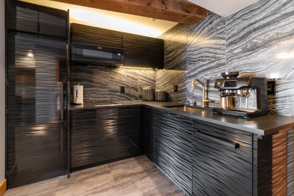 Sleek modern black kitchen featuring wavy cabinetry, marble wall, and elegant gold accents.