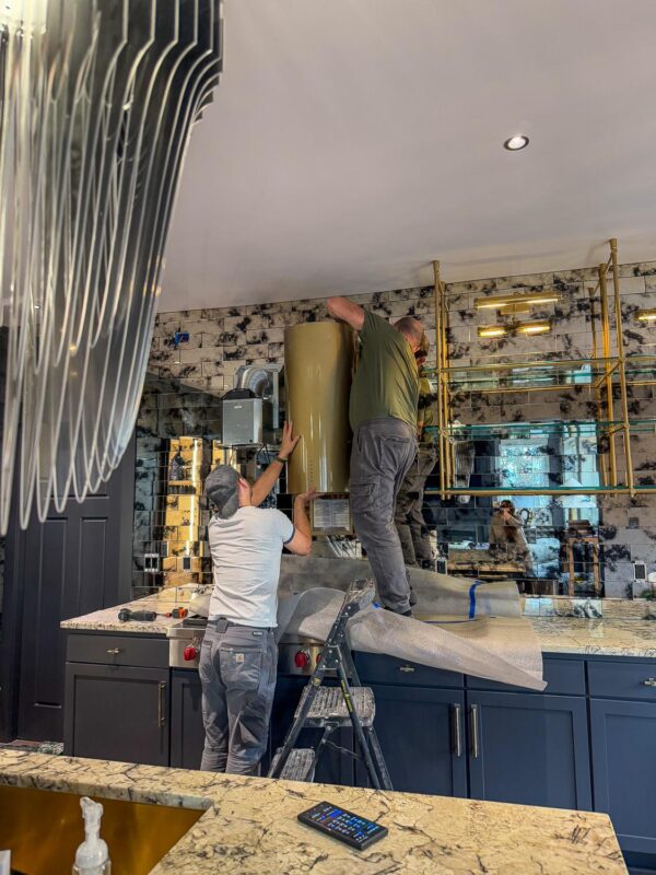 Kitchen renovation crew installs modern hood in stylish contemporary kitchen with navy cabinetry.
