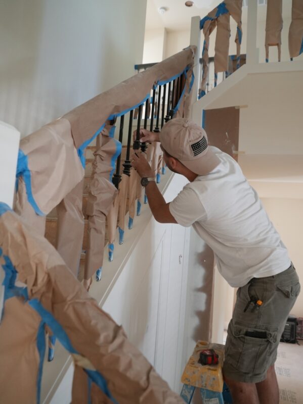 Man working on a staircase railing renovation with tools and painters tape.