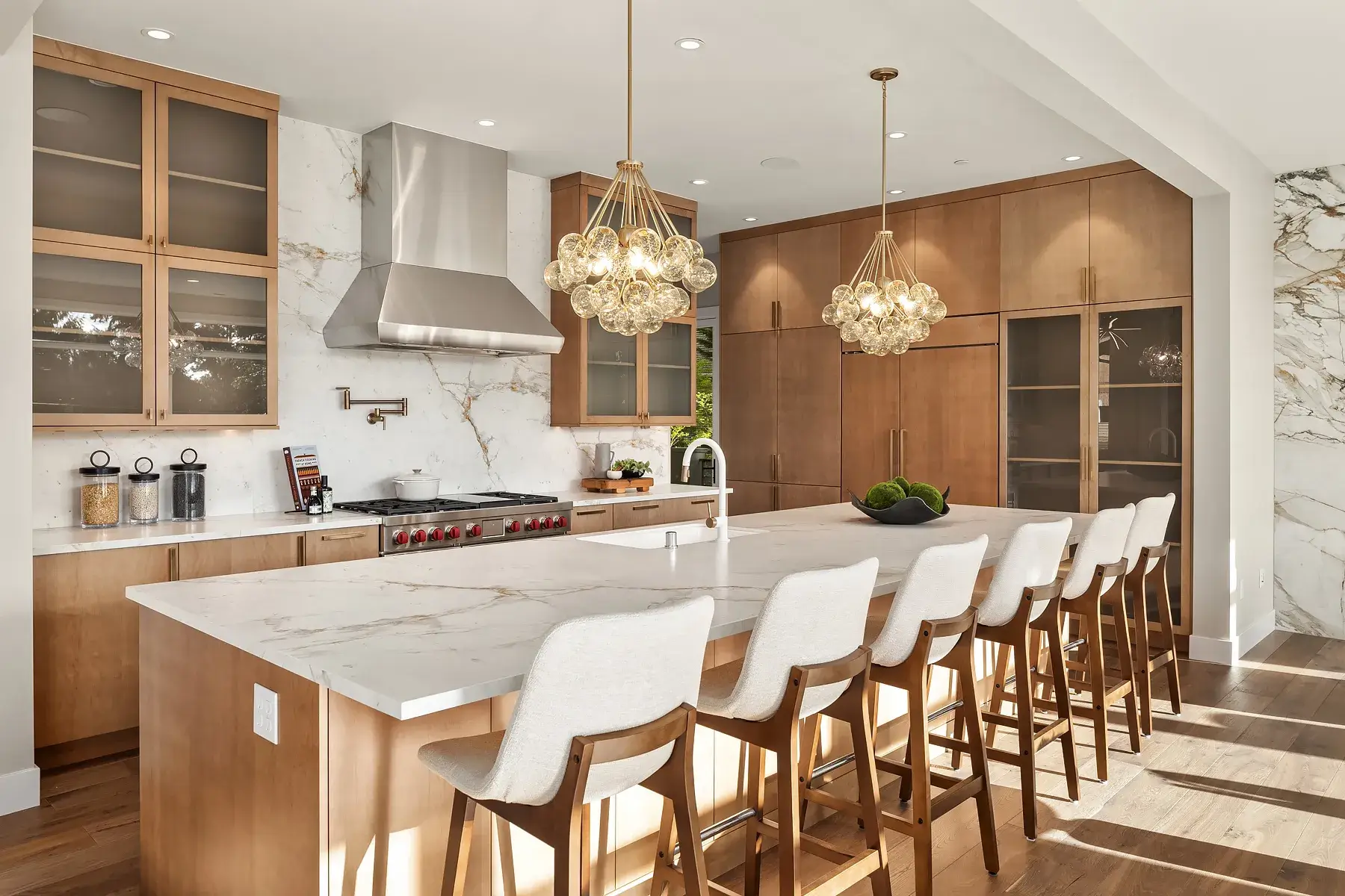 Stunning modern kitchen remodel by ARIID Build & Remodel featuring warm wood cabinetry, marble backsplash, island seating, and designer pendant lights